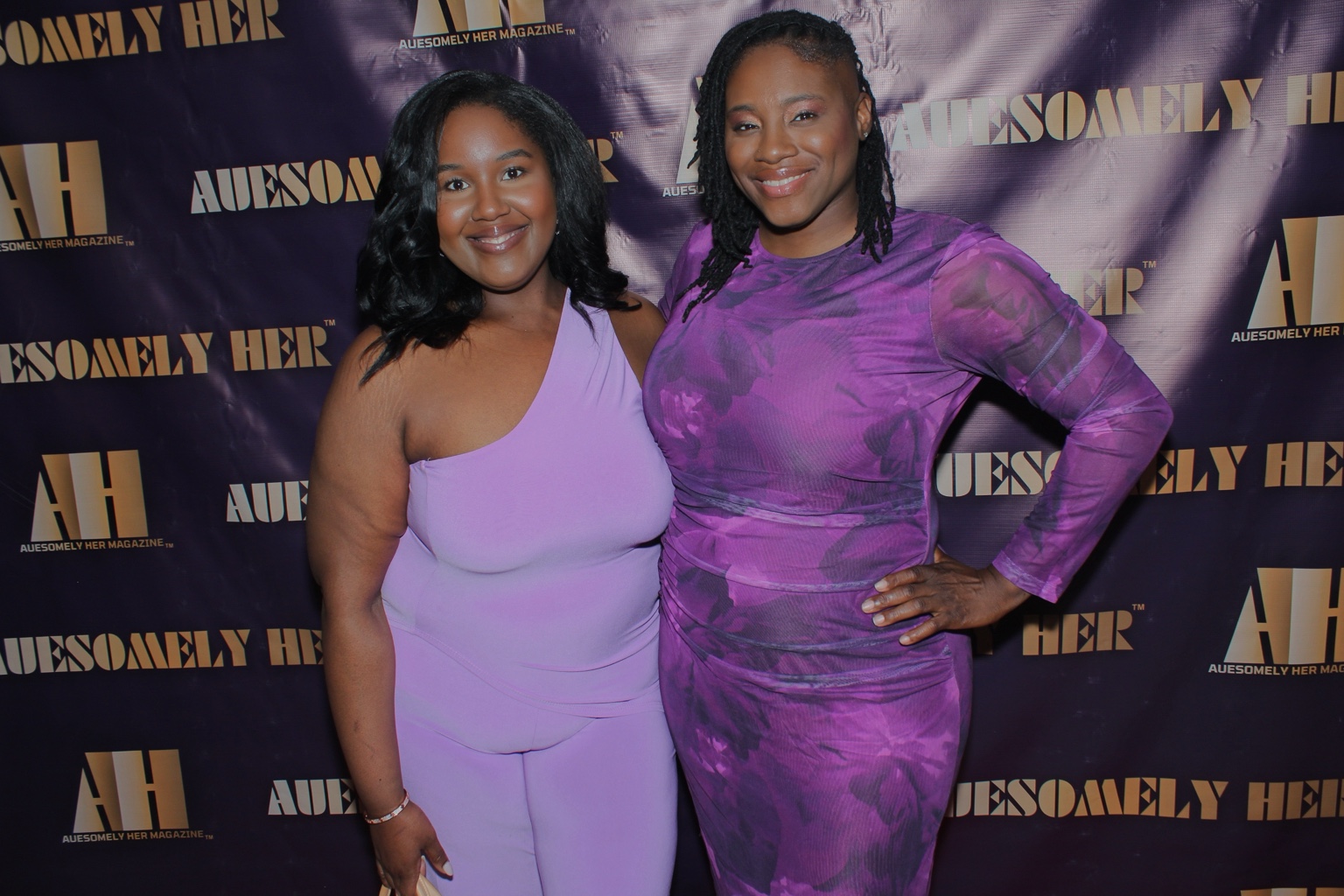 Two guests smiling in front of an Auesomely Her event backdrop