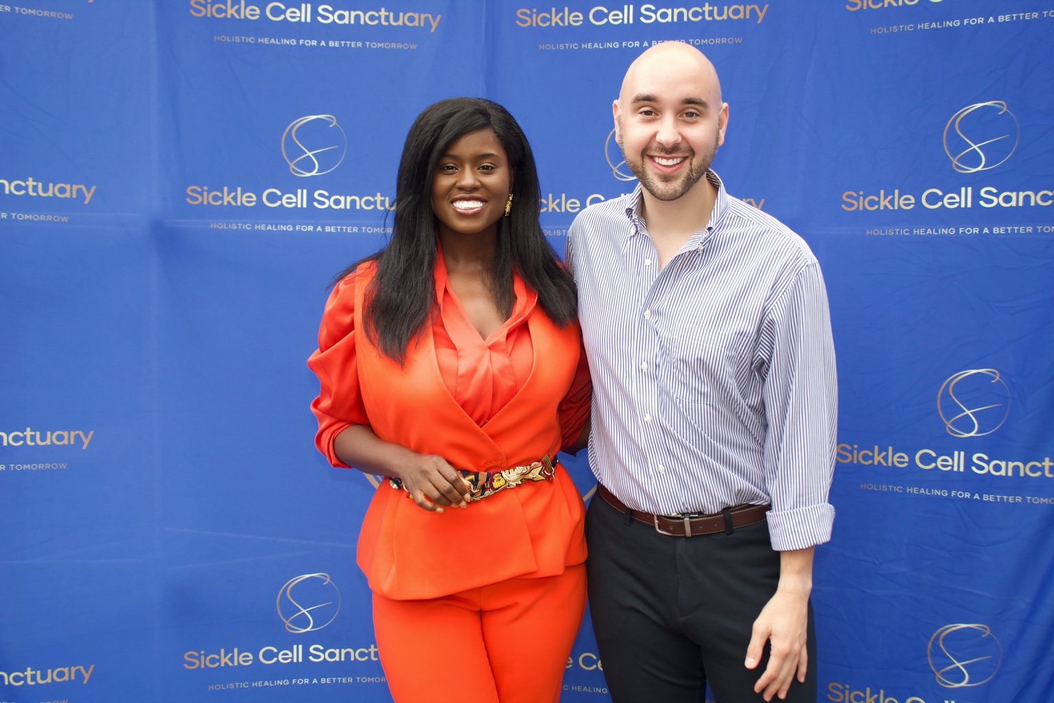 Two guests posing in front of a Sickle Cell Sanctuary backdrop