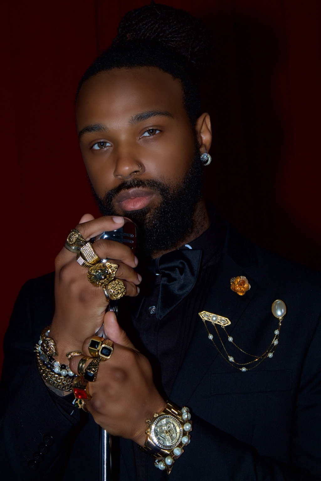 Man in a black suit and bow tie posed against a deep red background