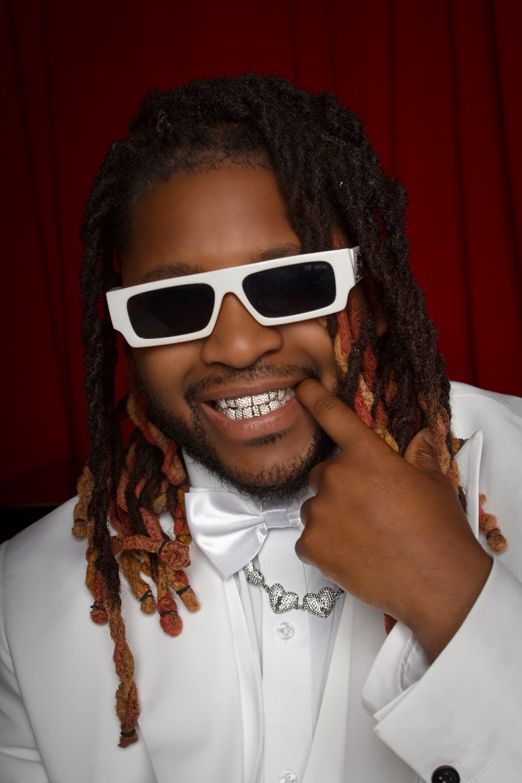 Smiling man in a white suit and sunglasses against a deep red background