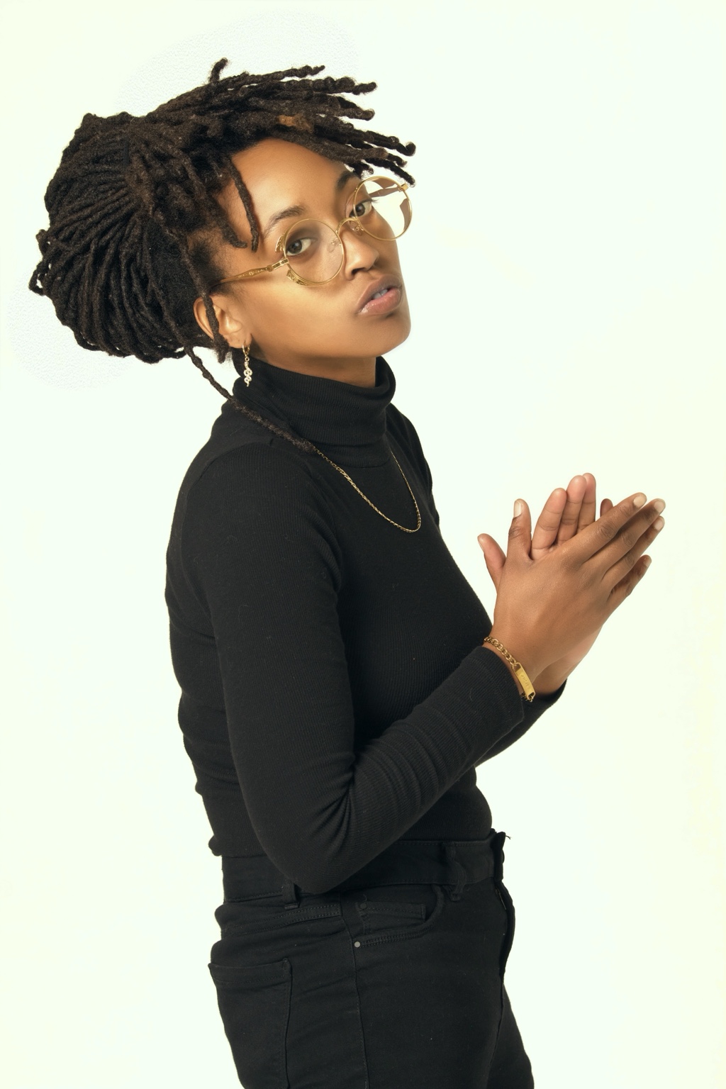 Ki wearing glasses and a black outfit against a light studio background