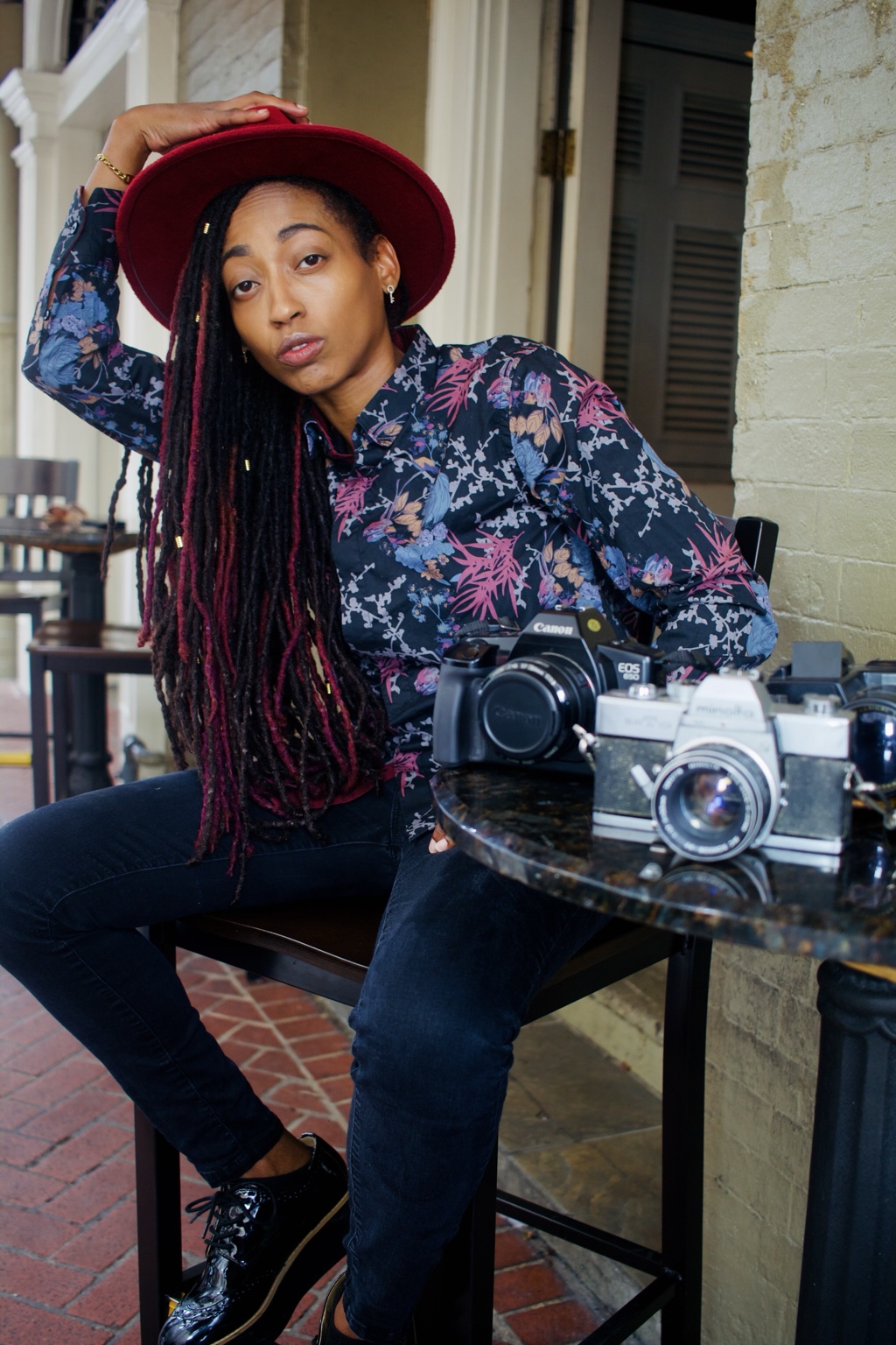 Ki seated beside her cameras wearing a burgundy hat